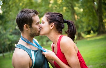 Young happy fitness couple kissing - woman put skipping rope around men's neck