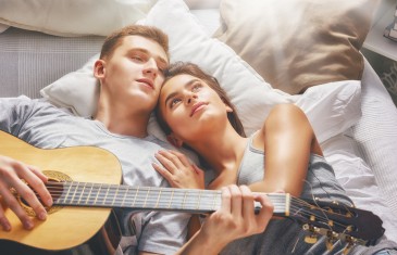 Happy couple in love. Stunning sensual portrait of young stylish fashion couple indoors. Young man playing guitar for his beloved girl.