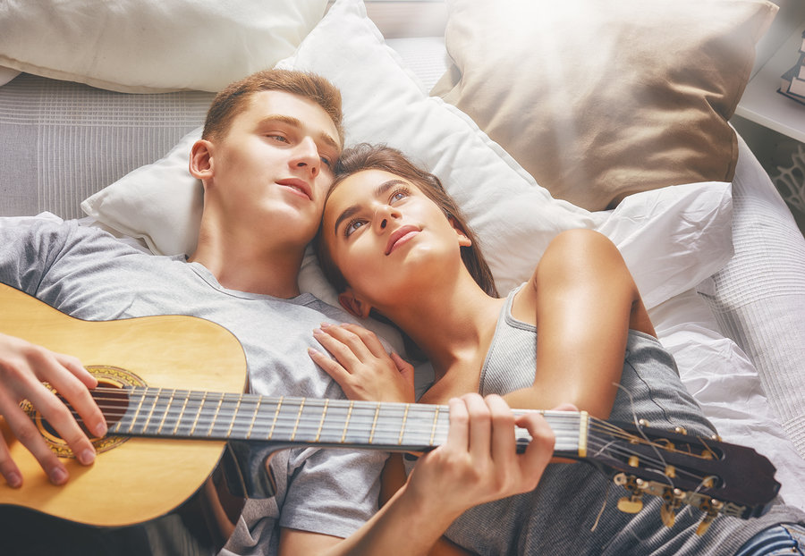 Happy couple in love. Stunning sensual portrait of young stylish fashion couple indoors. Young man playing guitar for his beloved girl.