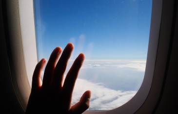 Silhouette of woman hand over the window of airplane. Clouds and sky as seen through window of an aircraft air plane.
