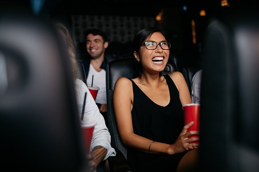 Shot of young woman sitting in multiplex movie theater watching movie and laughing.