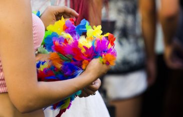 Close up on arms of unidentifiable woman holding colorful bouquet of feathers in a crowd