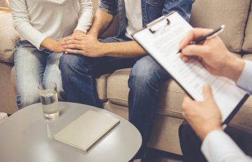 At the psychologist. Cropped image of beautiful young couple sitting on couch and holding hands while doctor is making notes