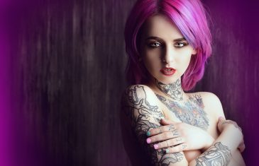 Beautiful young woman with stylish crimson hair and tattoo on her body posing over dark grunge background. Hair coloring. Cosmetics, make-up. Tattoo.