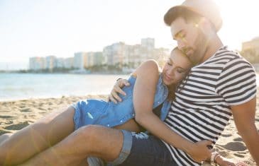 young happy couple sitting on beach cuddling