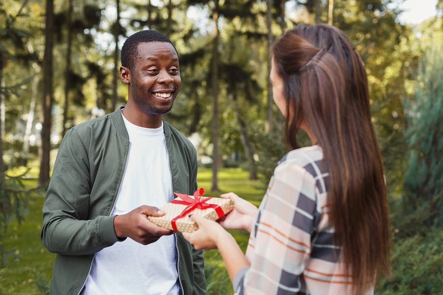 Young asian woman with giftbox surprising her african-american boyfriend